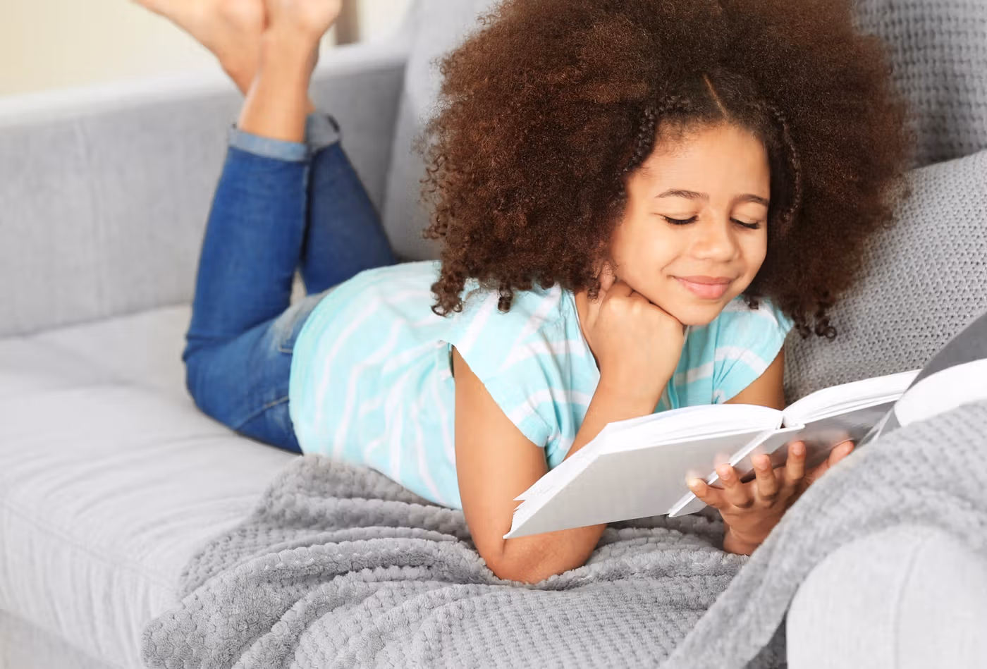 Meisje met krullen leest op de bank een boek