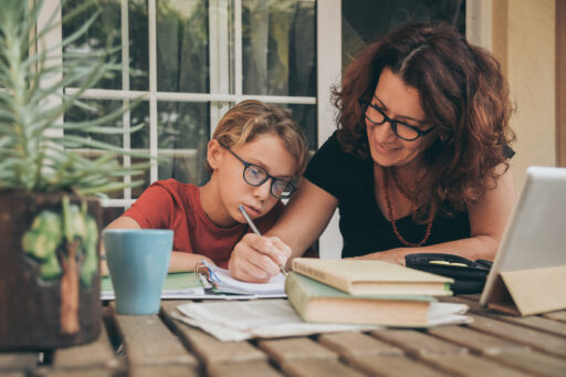 Moeder helpt zoon bij het maken van huiswerk. Ze zitten samen aan tafel en moeder legt het uit.